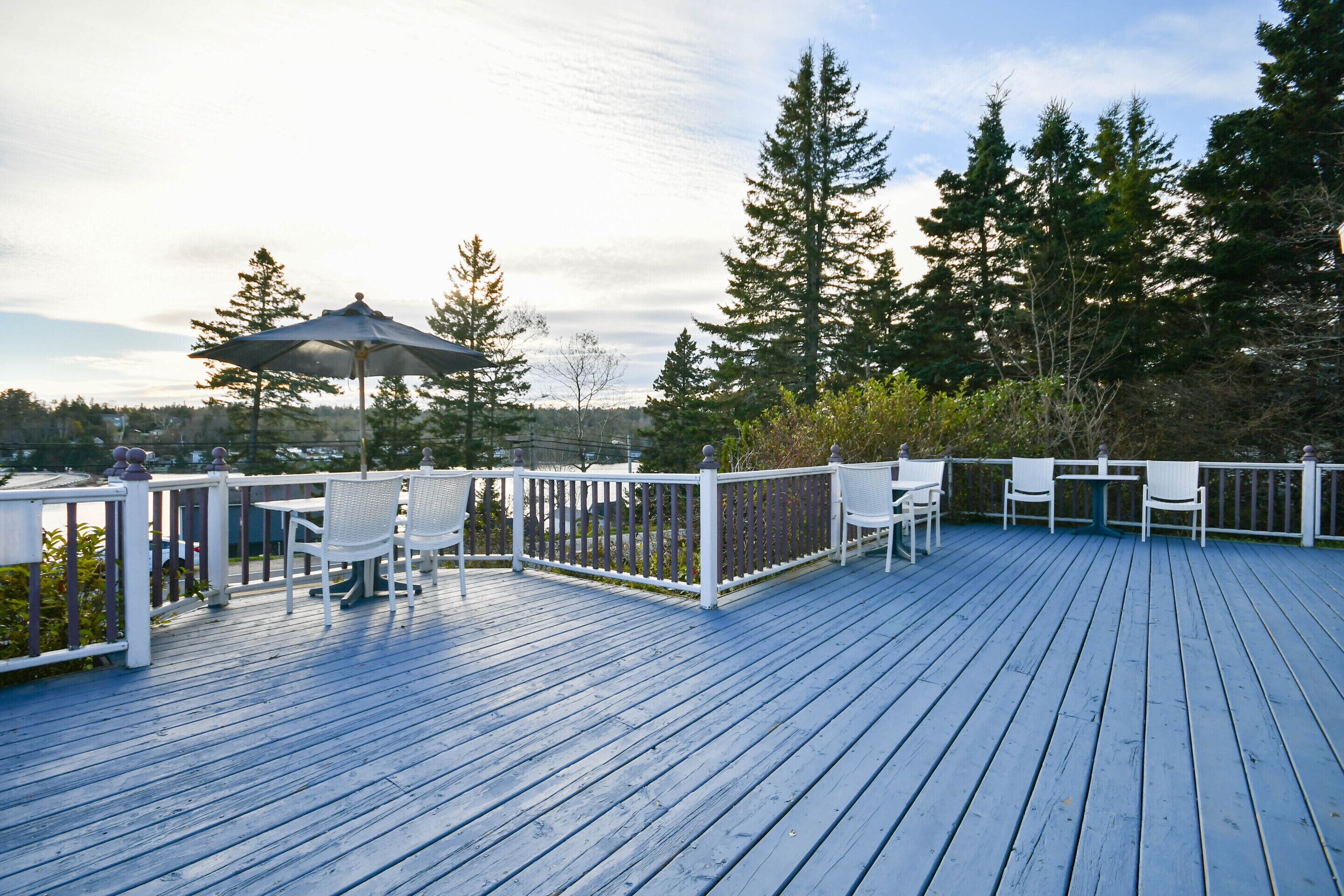 A wooden deck with white railings and seating, overlooking a forested area.