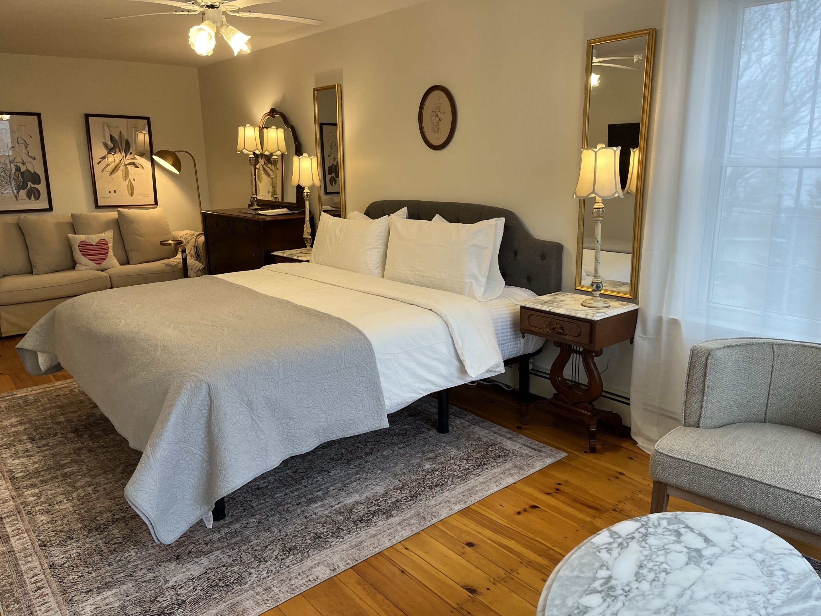 Un dormitorio ordenado con una cama grande, mesitas de noche, una silla y una mesa redonda.
