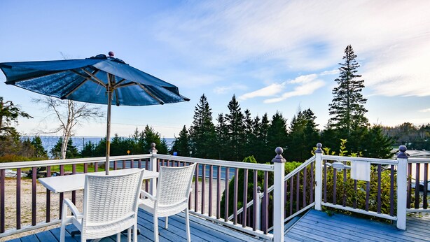 A deck with a table and chairs, a blue umbrella, and a railing overlooking a body of water and trees. - Surfside Inn (Queensland)