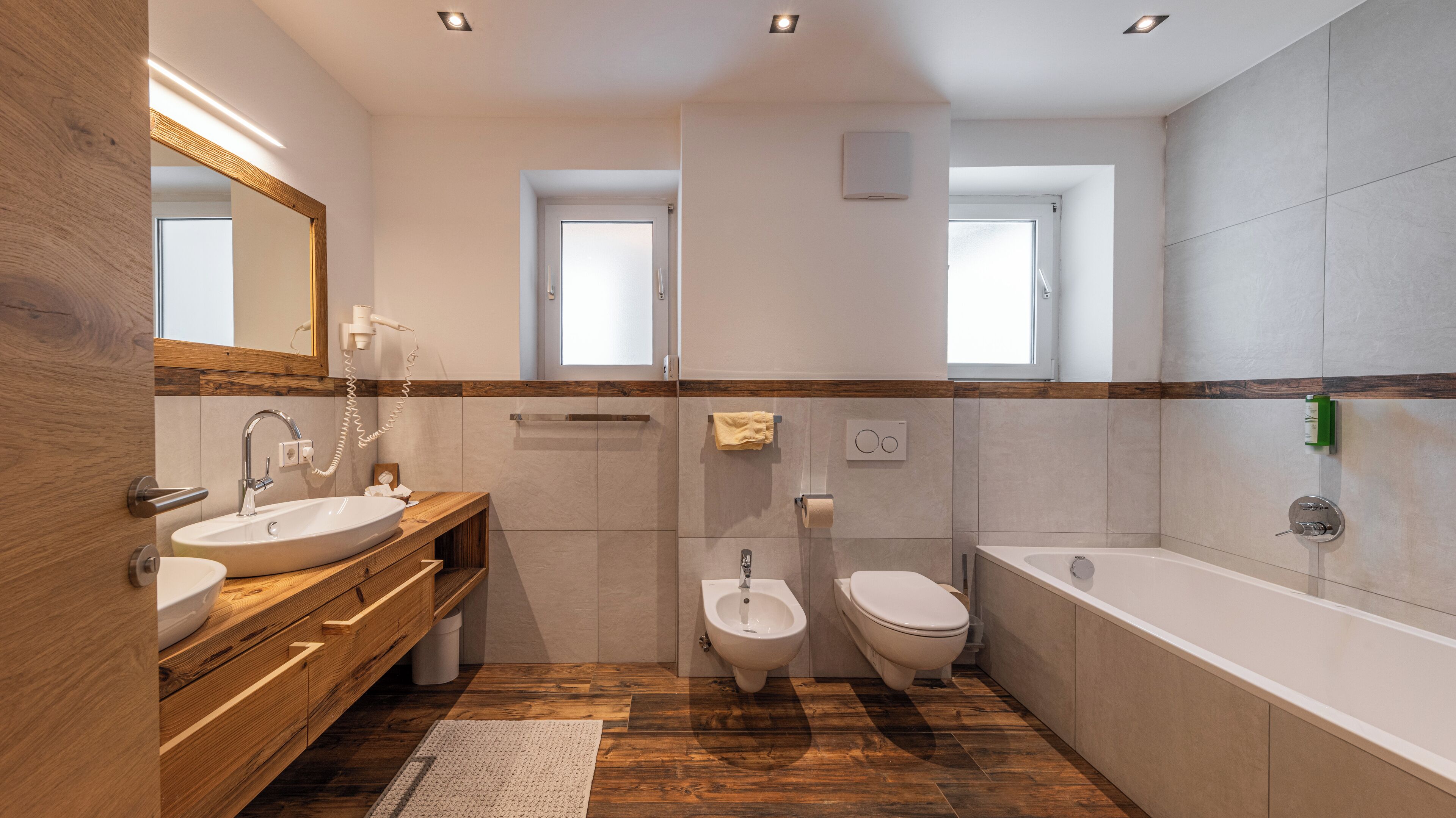 A modern bathroom with a wooden vanity, a bidet, a toilet, and a bathtub.