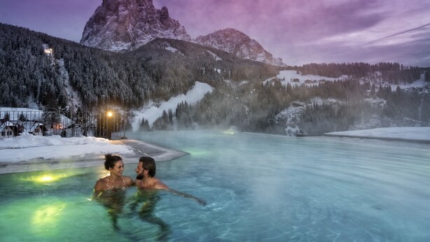 A couple in a clear, blue pool with a mountainous backdrop. - Hotel Interski (Santa Cristina Val Gardena)