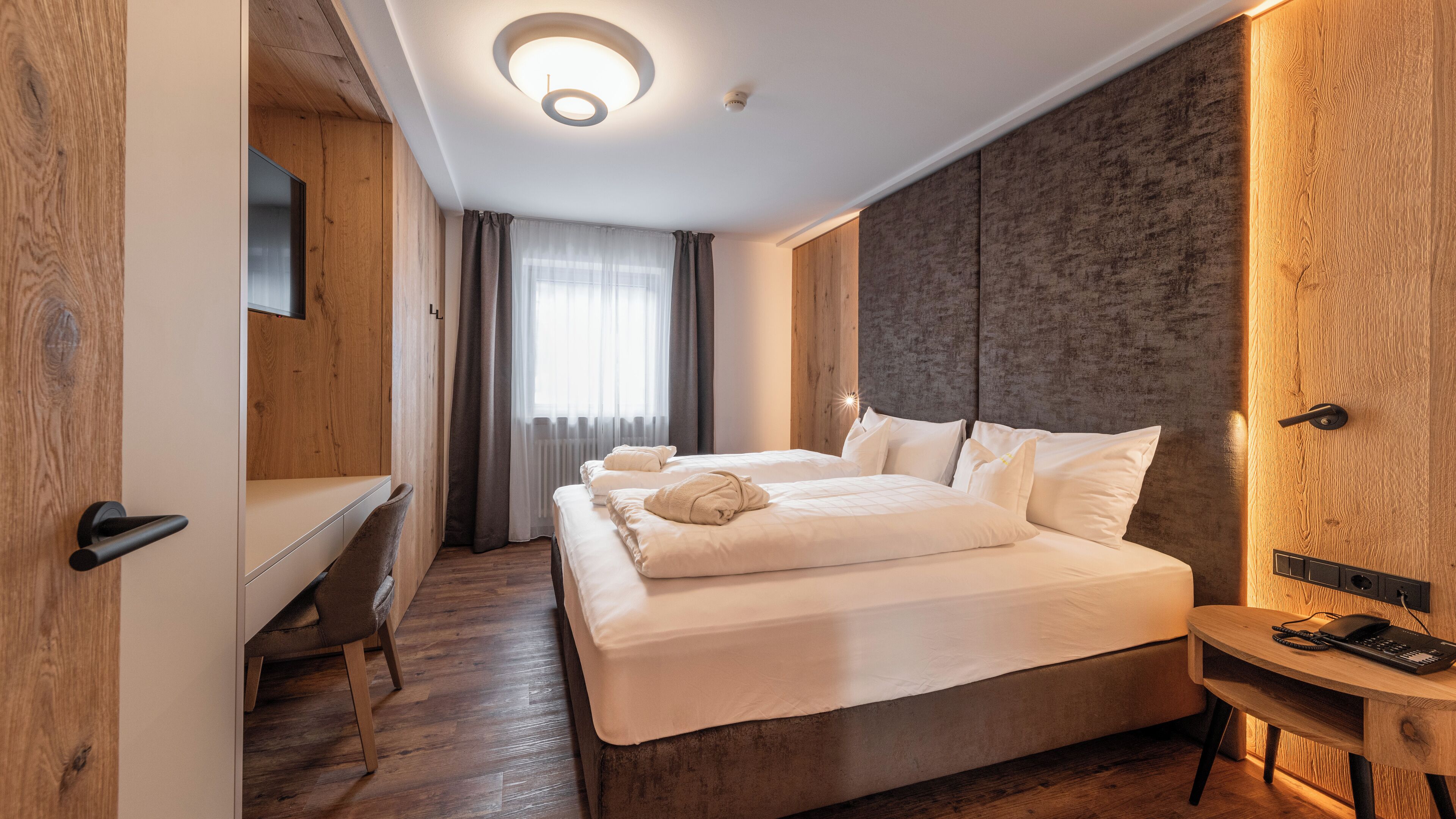 A modern hotel room with a large bed, a desk, and a small table with a phone.
