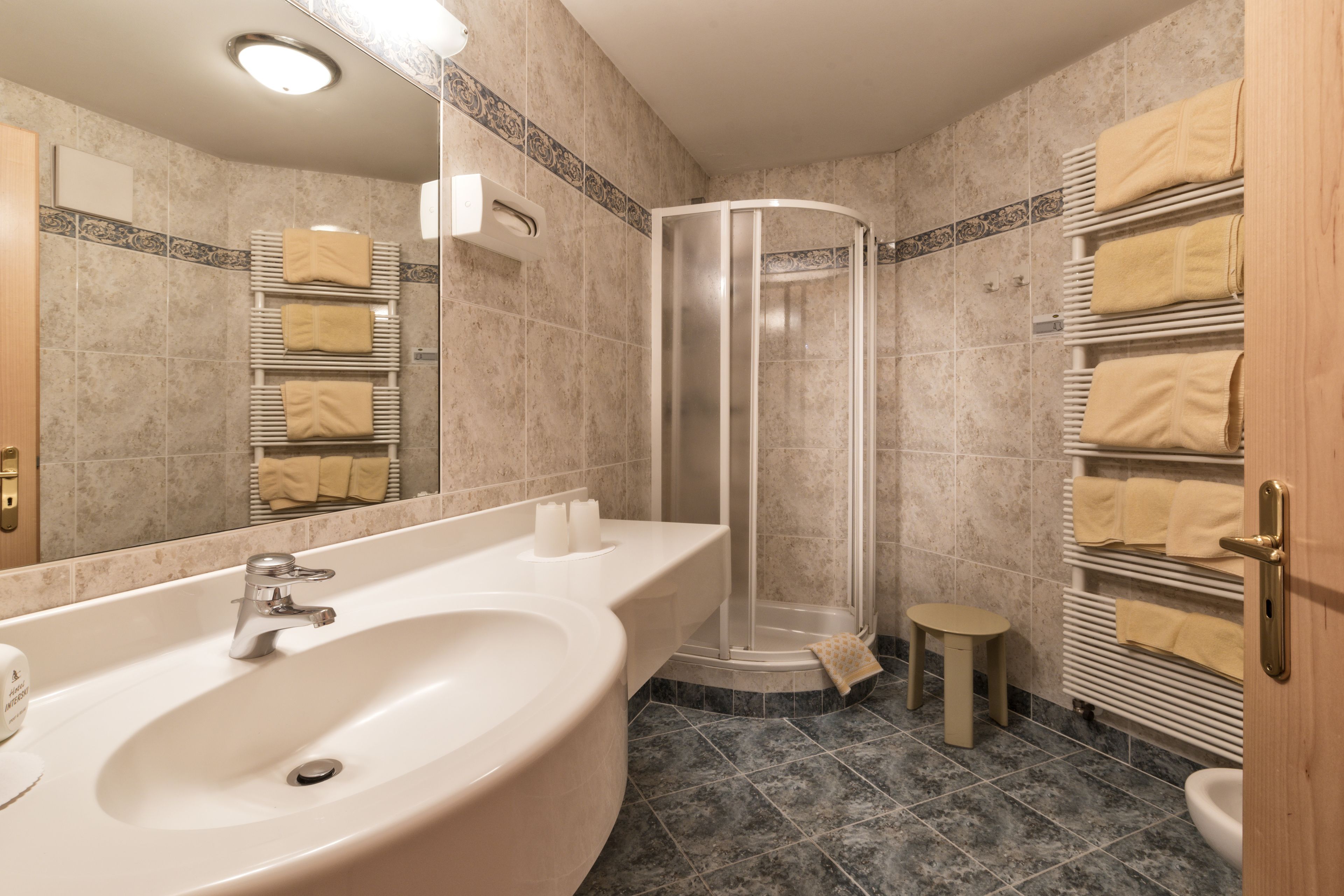 Un baño moderno con un lavamanos grande, cabina de ducha de vidrio y un perchero con toallas dobladas con cuidado.