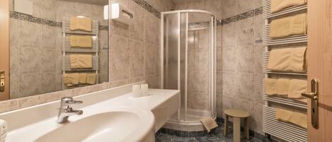 Un baño moderno con un lavamanos grande, cabina de ducha de vidrio y un perchero con toallas dobladas con cuidado.