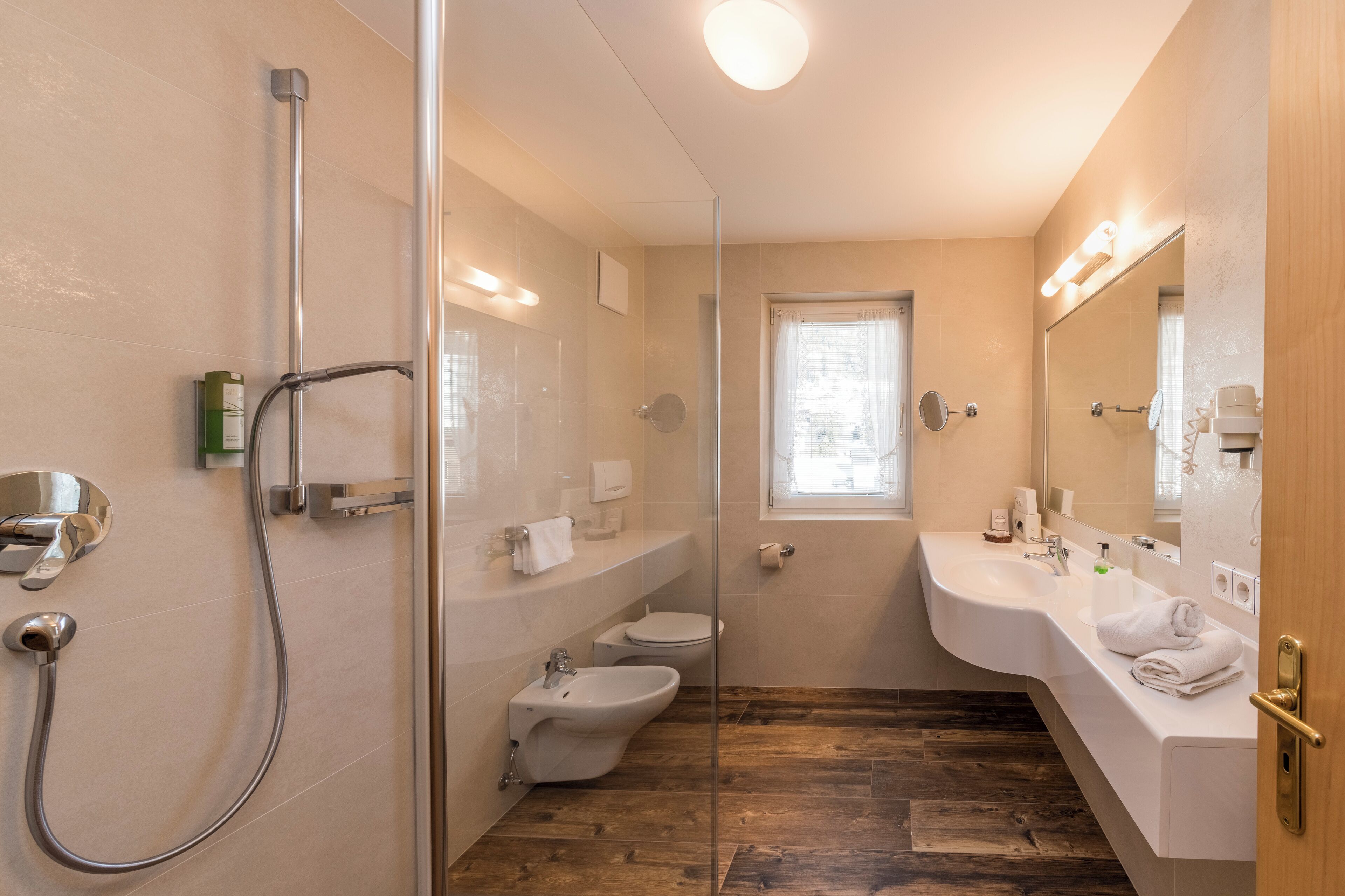 Un baño moderno con cabina de ducha de vidrio, un bidé, un inodoro y un lavabo con espejo.