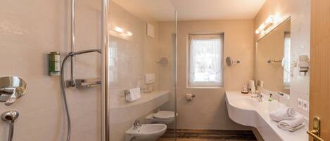 Un baño moderno con cabina de ducha de vidrio, un bidé, un inodoro y un lavabo con espejo.