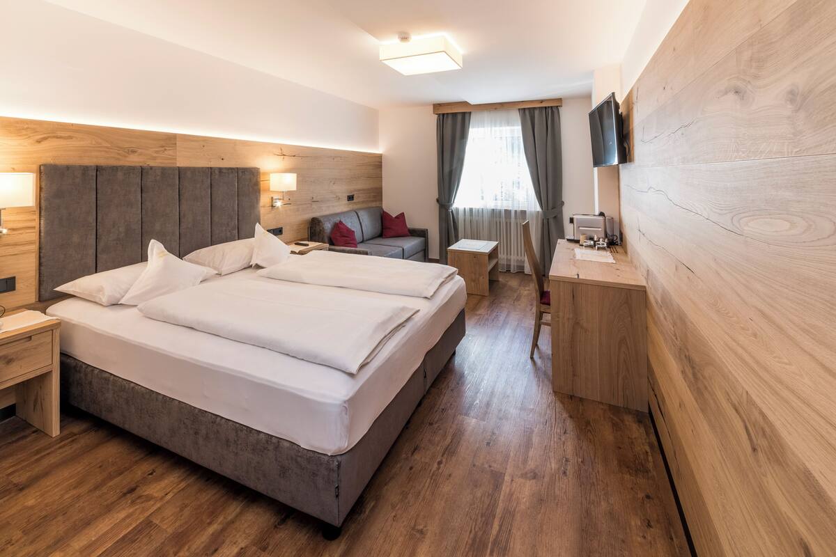 Una habitación de hotel con una cama grande, un escritorio, un televisor y una ventana con cortinas.