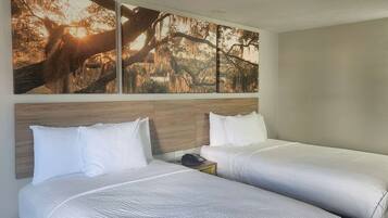 A hotel room with two beds, a wooden headboard, a nightstand with a phone, and a large wall mural of a tree.
