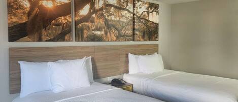 A hotel room with two beds, a wooden headboard, a nightstand with a phone, and a large wall mural of a tree.