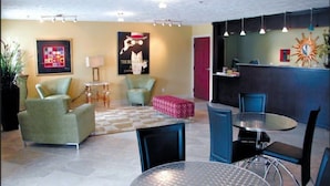 Un soggiorno moderno con un tappeto a scacchi, poltrone verdi, un poggiapiedi rosso, un tavolino rotondo in metallo e una zona pranzo blu.