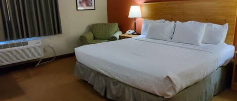 Una habitación de hotel con una cama, una silla, una lámpara y un equipo de aire acondicionado.