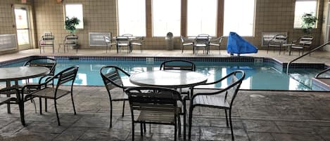 An indoor swimming pool with tiled walls, multiple seating areas, and a covered section.