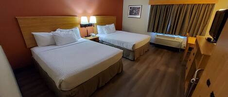 Une chambre d’hôtel avec deux lits, un bureau, une chaise, une télévision et une fenêtre avec des rideaux.