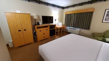 Een hotelkamer met een groot bed, een houten bureau, een televisie, een stoel en een raam met gordijnen.