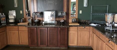 A kitchen with wooden cabinets, a chalkboard, a coffee machine, and a buffet area.