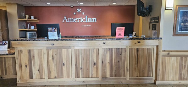 A reception desk at AmericInn with a wooden counter, a television, and a sign indicating no smoking.