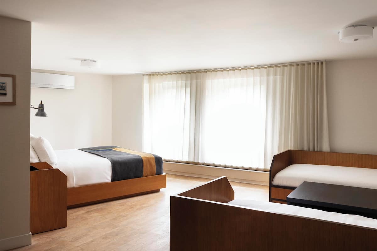 A hotel room with a bed, a sofa, a desk, and a large window with curtains.