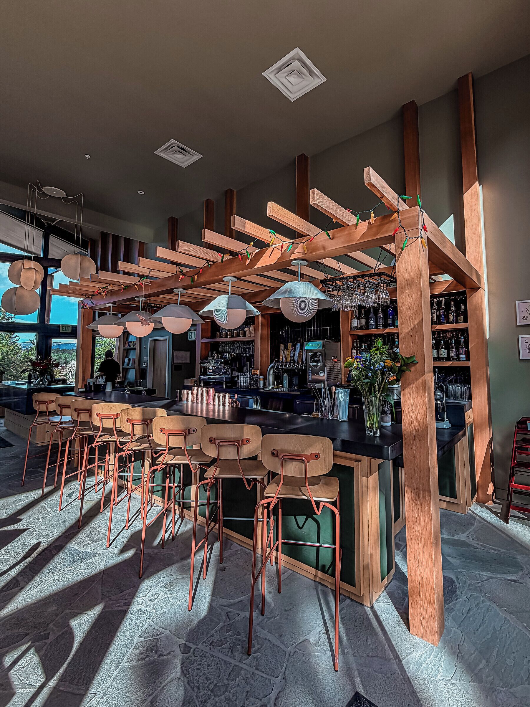 Una zona de bar con vigas de madera, taburetes y una barra.