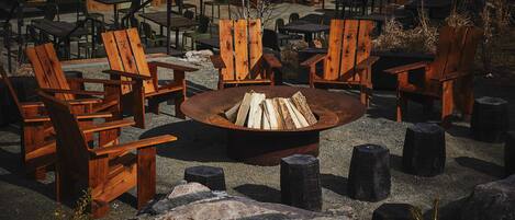 A rustic outdoor seating area with wooden chairs and a central fire pit.