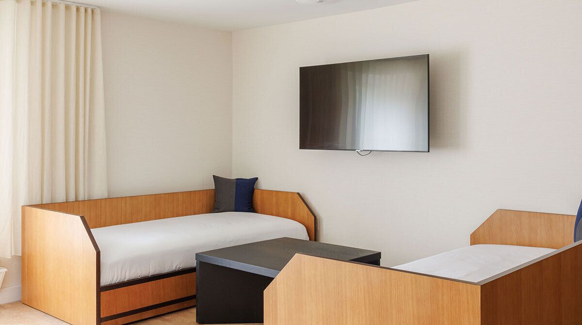 A modern hotel room with a wooden sofa, a small table, and a flat-screen TV mounted on the wall.