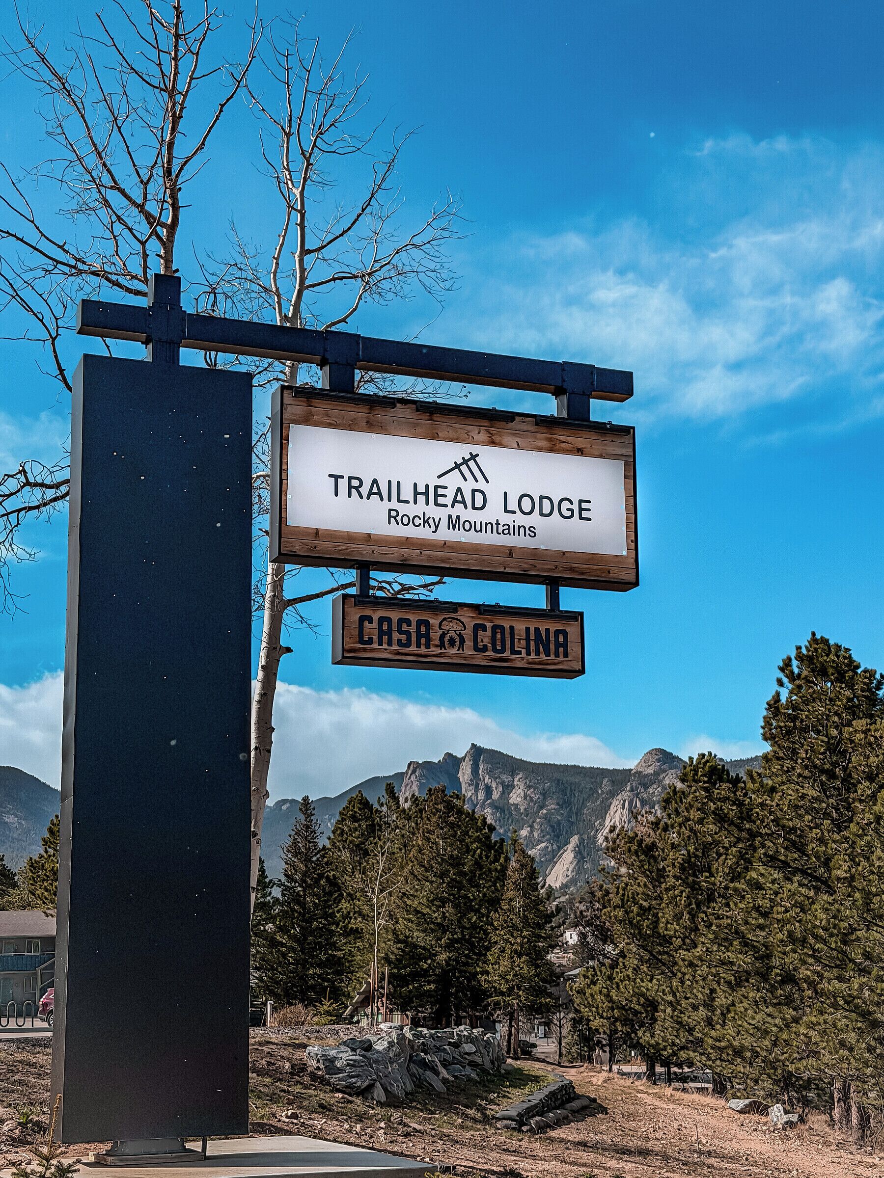 A sign for Trailhead Lodge in Rocky Mountains with a view of mountains in the background.