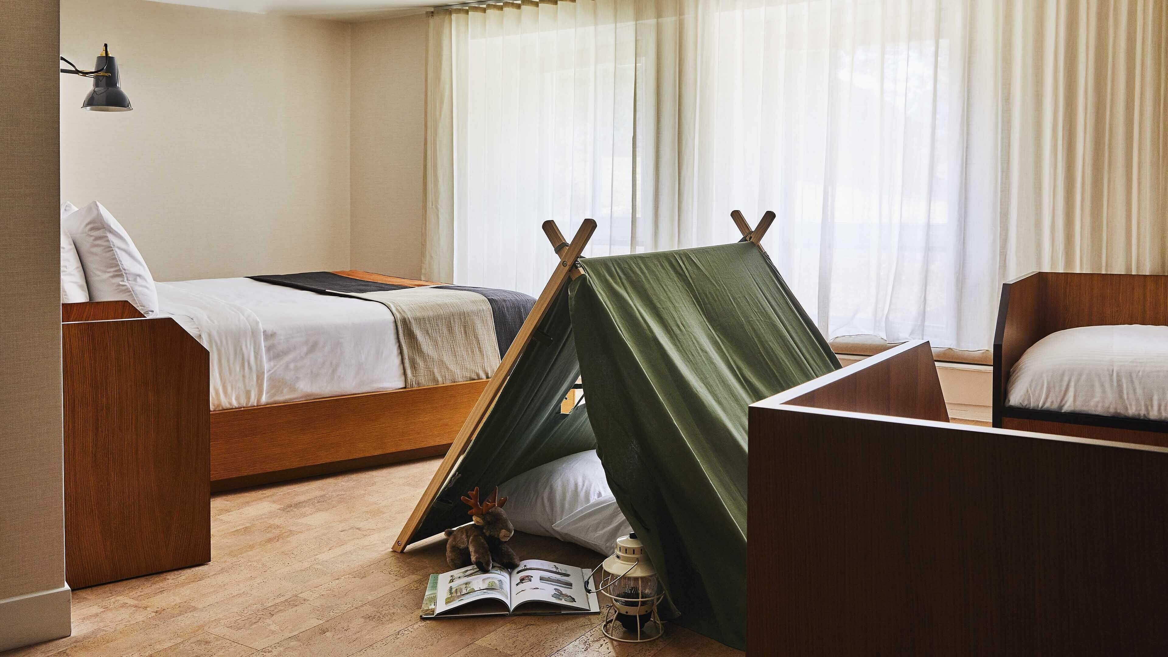 A bedroom with a bed, a green tent-like structure, a lamp, and a book on the floor.