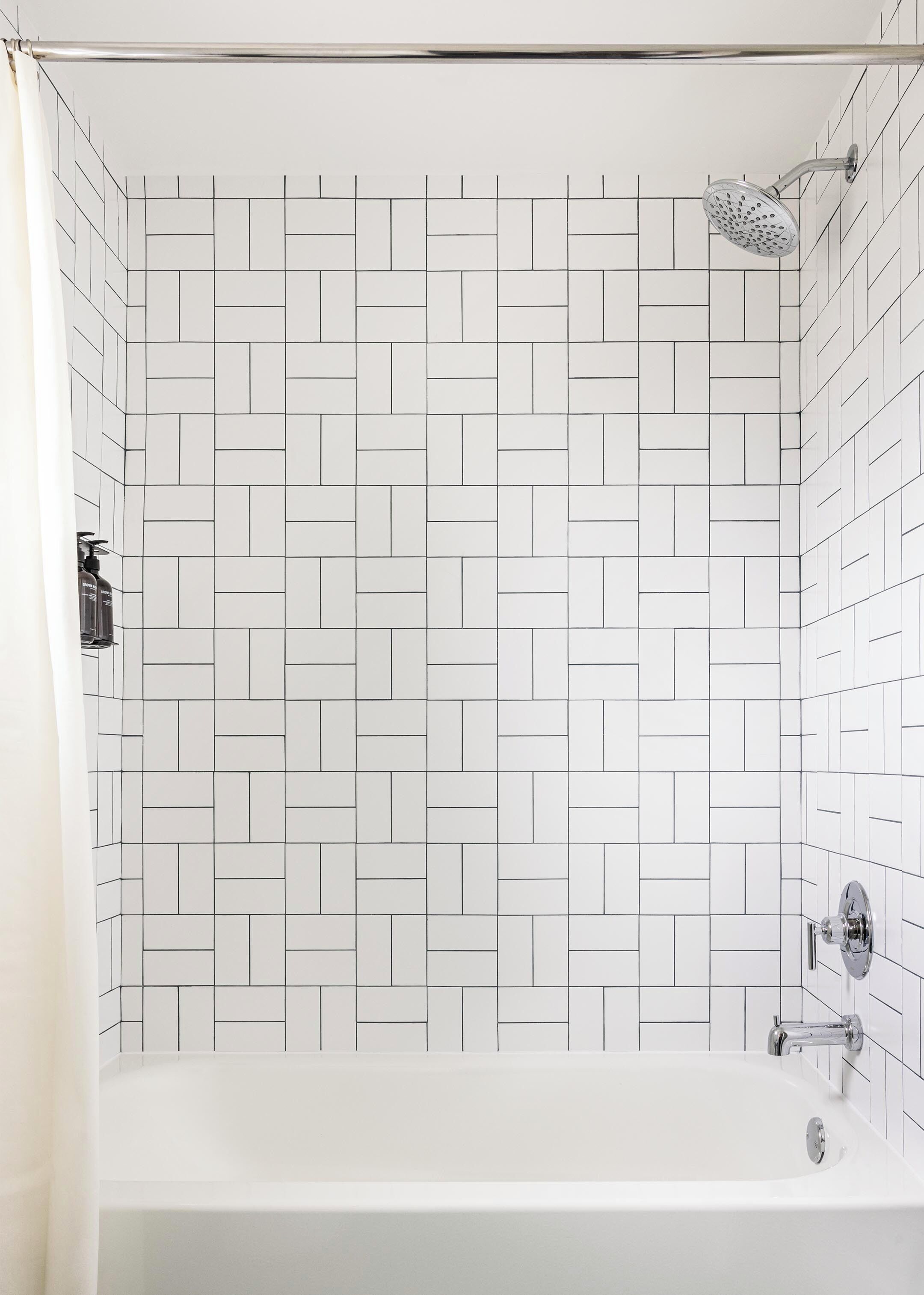 A modern bathroom with a white tiled wall, a bathtub, and a showerhead.