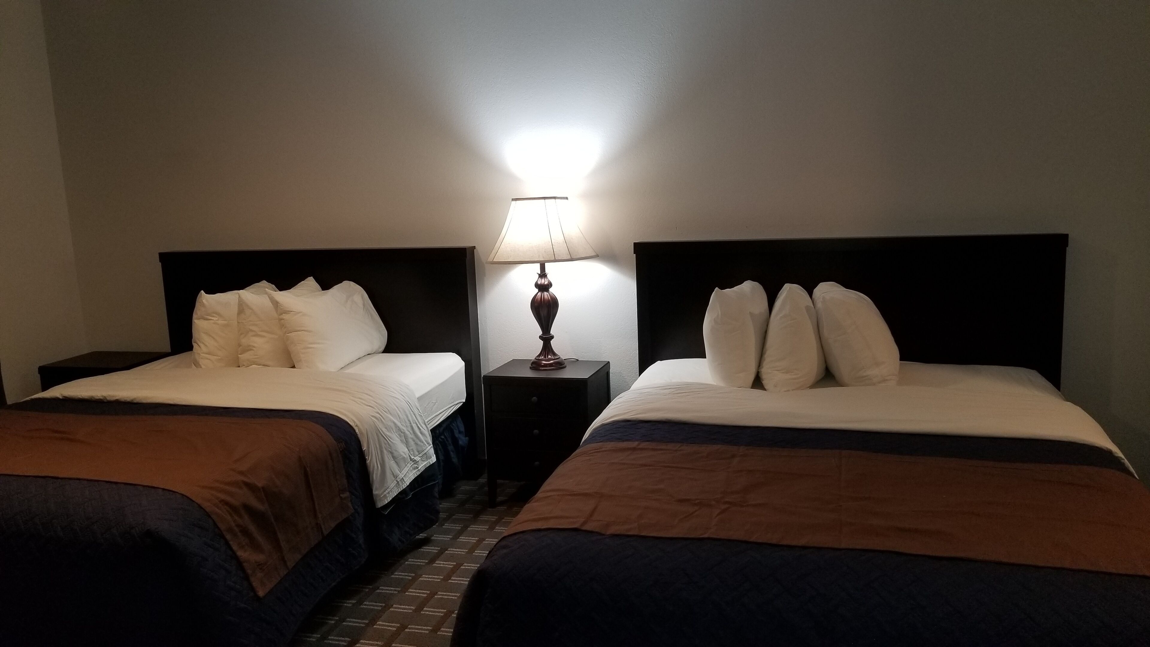 Une chambre d’hôtel avec deux lits, chacun doté de draps blancs et d’une tête de lit marron. Une table de chevet avec une lampe se trouve entre les deux lits.