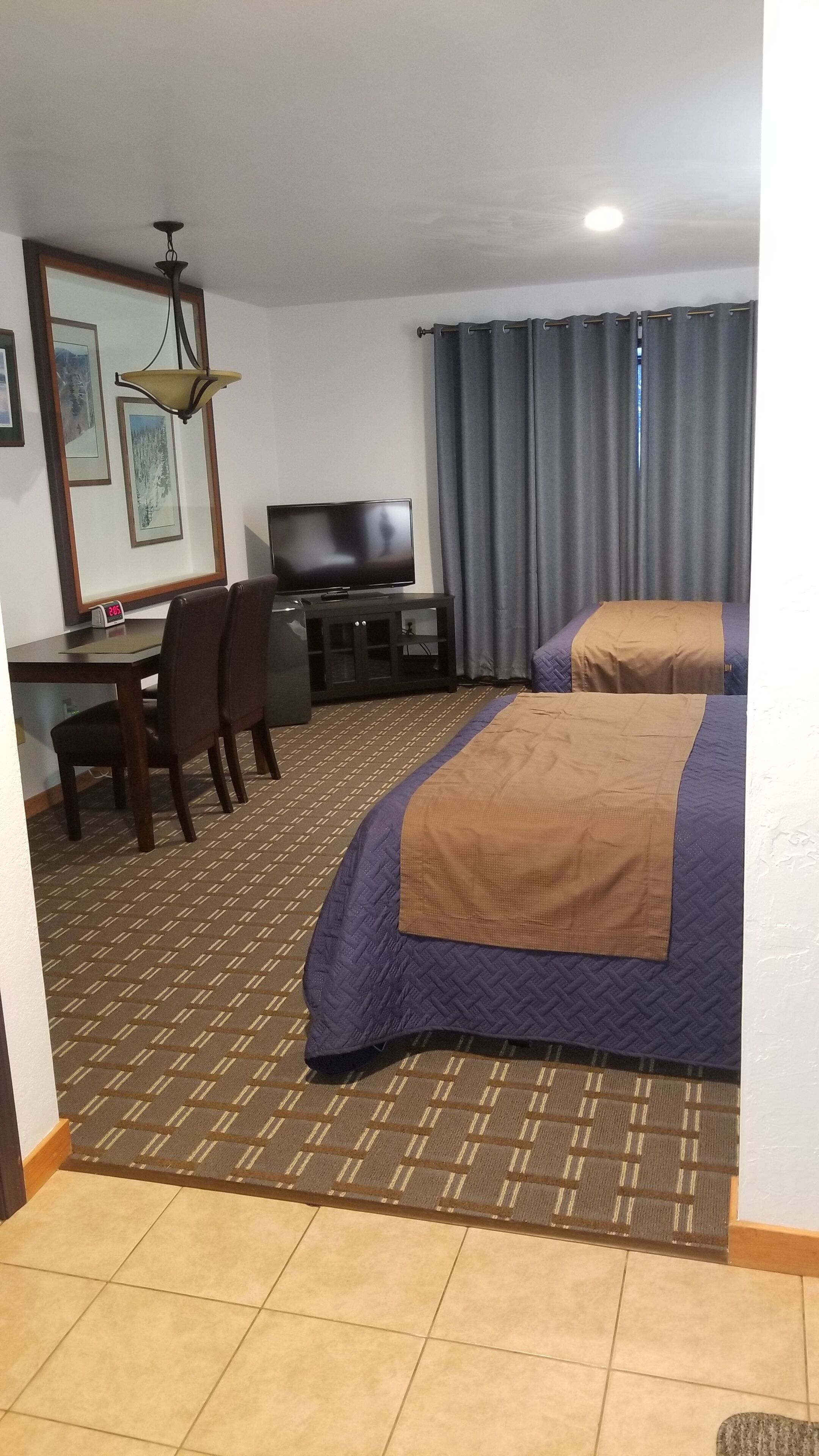 Ein Hotelzimmer mit Bett, Schreibtisch mit Stuhl, Fernseher und einer Uhr.