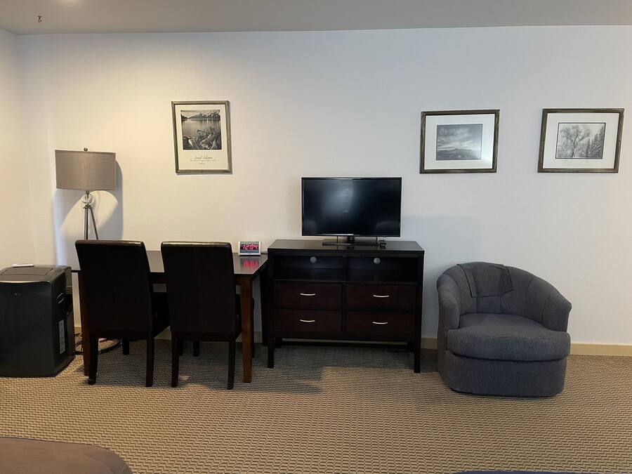 Habitación de hotel con escritorio, dos sillas, televisión, lámpara y tres cuadros en la pared.