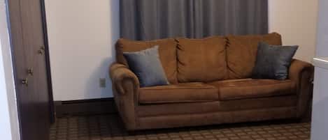 A room with a brown sofa, patterned rug, and a grey curtain.