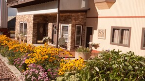 A two-story building with a stone facade, a balcony with a railing, and a flower bed with various flowers. - Valley Hi Motel - Near Winter Park Visitor Center (Winter Park)