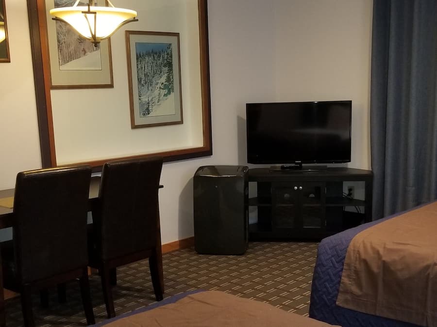 Habitación de hotel con cama, escritorio con sillas, televisión y cuadros en la pared.