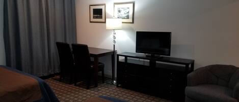 A hotel room with a bed, a desk with a chair, a TV, and a lamp.