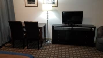 A hotel room with a bed, a desk with two chairs, a TV on a stand, a lamp, and a dresser.