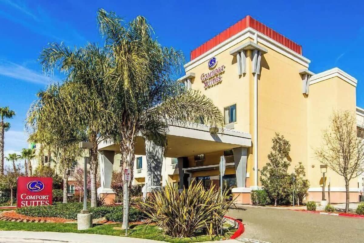A hotel with a yellow facade, a red roof, and a sign reading 'Comfort Suites.'