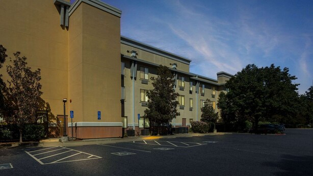 A multi-story hotel with a parking lot, trees, and a clear sky. - Comfort Suites Vacaville-Napa Valley Area (Vacaville)