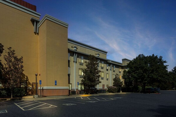 A multi-story hotel with a parking lot, trees, and a clear sky.