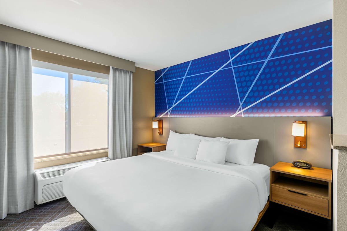 A hotel room with a large bed, two bedside tables with lamps, a wall-mounted light, and a window with curtains.