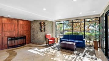 Un hall con pared de piedra, paneles de madera, un sillón rojo, un sofá azul y un ventanal con vistas a árboles.