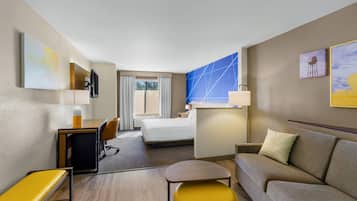 A hotel room with a bed, a sofa, a desk with a chair, a small table, and a TV mounted on the wall.