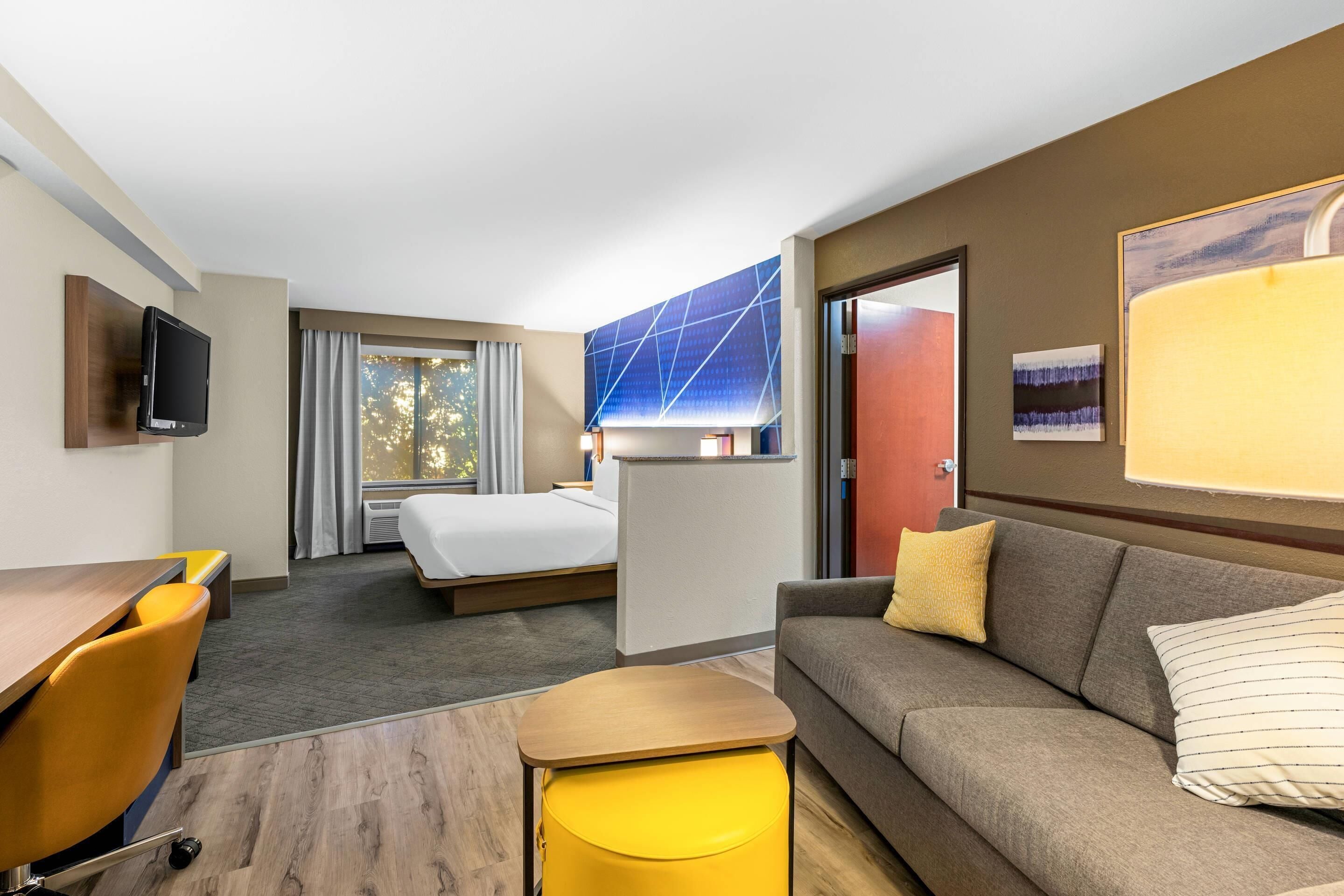 A hotel room with a bed, a sofa, a desk, a TV, and a window with curtains.