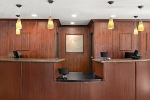 Zona de recepción con paneles de madera, dos mostradores y un reloj, con iluminación colgante.