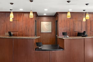 Zona de recepción con paneles de madera, dos mostradores y un reloj, con iluminación colgante.