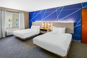 Habitación de hotel con dos camas, una ventana con cortinas, un muro con diseño geométrico y una puerta.