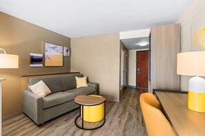 Ein Hotelzimmer mit einer Couch, einem kleinen runden Tisch, einem Holzstuhl und einem Bett.