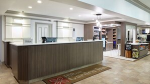 Un espace d’accueil moderne, avec un comptoir en bois, un terminal d’enregistrement numérique et un mini-bar.