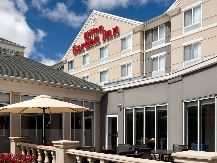 A Hilton Garden Inn exterior with a patio area featuring outdoor furniture and a large umbrella.