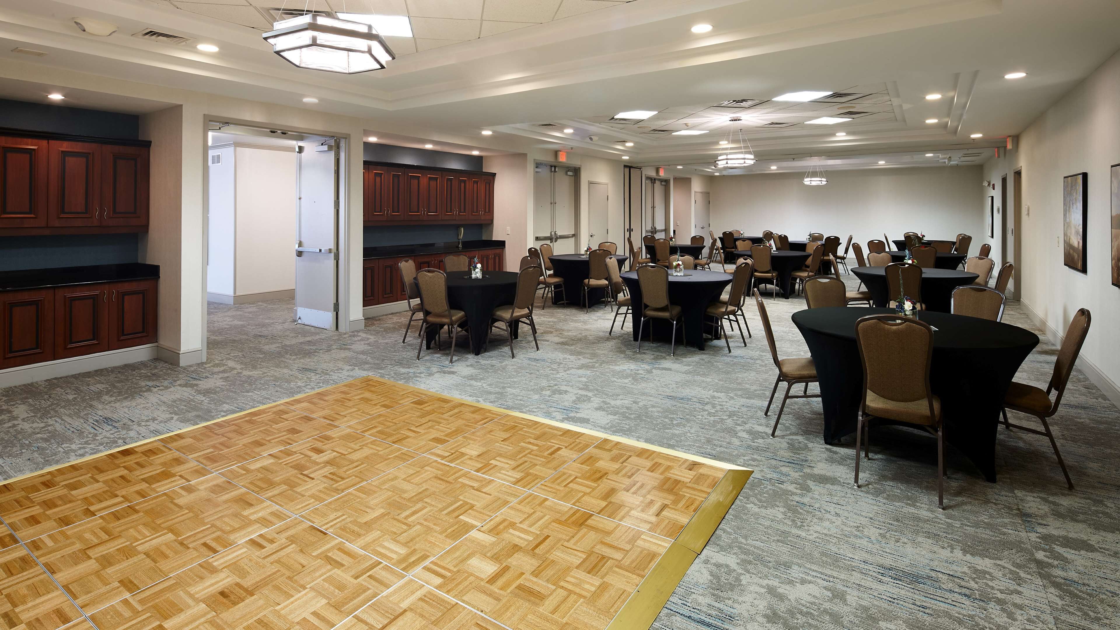 A spacious conference room with multiple tables and chairs, wooden flooring, and a large open area.