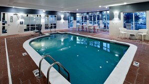 Une piscine avec vue sur le parking et les arbres à l’extérieur.